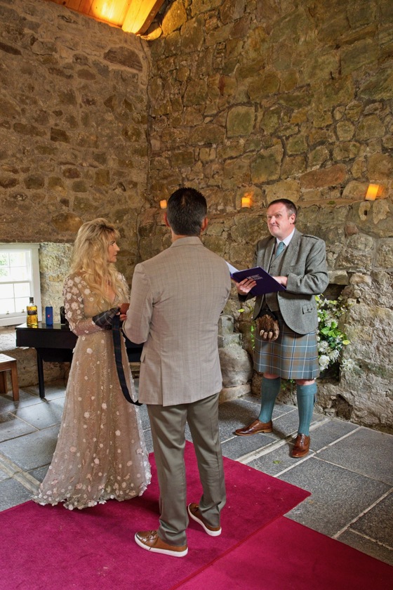 Bride and groom performing handfast with celebrant reading ceremony